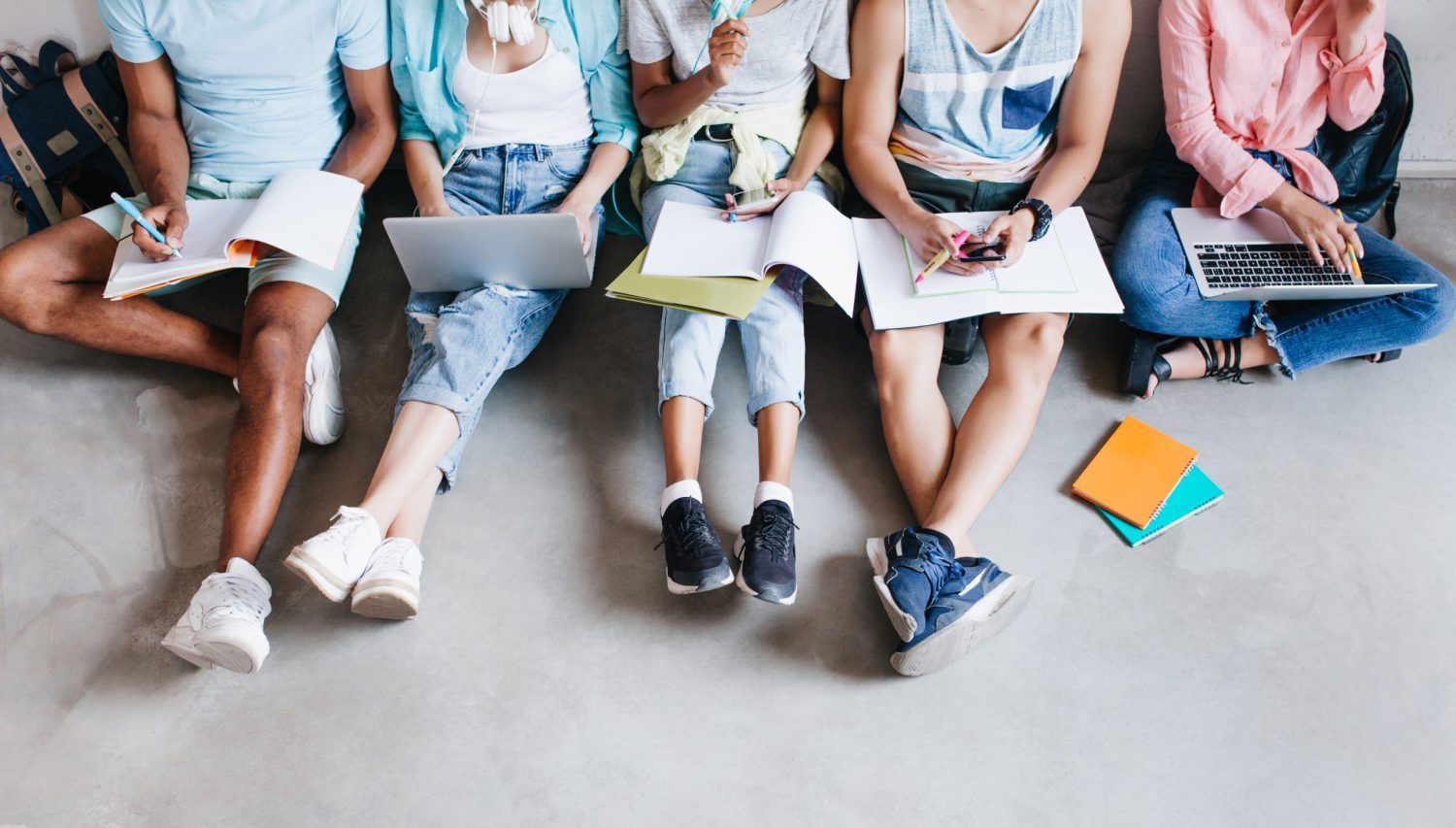 Overhead portrait of young people with laptops and smartphones, sitting together on the floor. Students writing lectures holding textbooks on their knees.. ritratto-dall-alto-di-giovani-con-laptop-e-smartphone-seduti-insieme-sul-pavimento-studenti-che-scrivono-lezioni-tenendo-i-libri-di-testo-sulle-ginocchia-